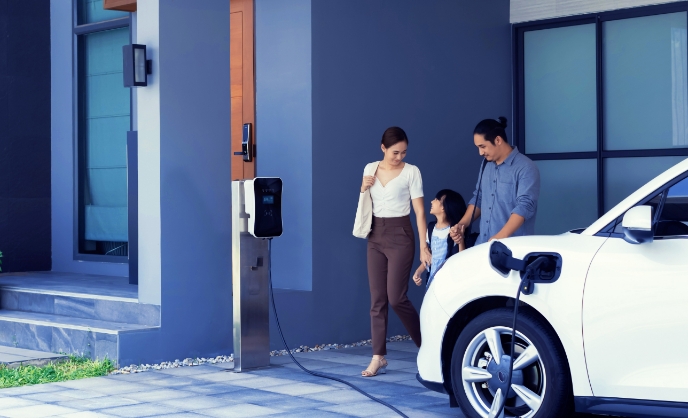 A family approaches their electric vehicle charging at a station.