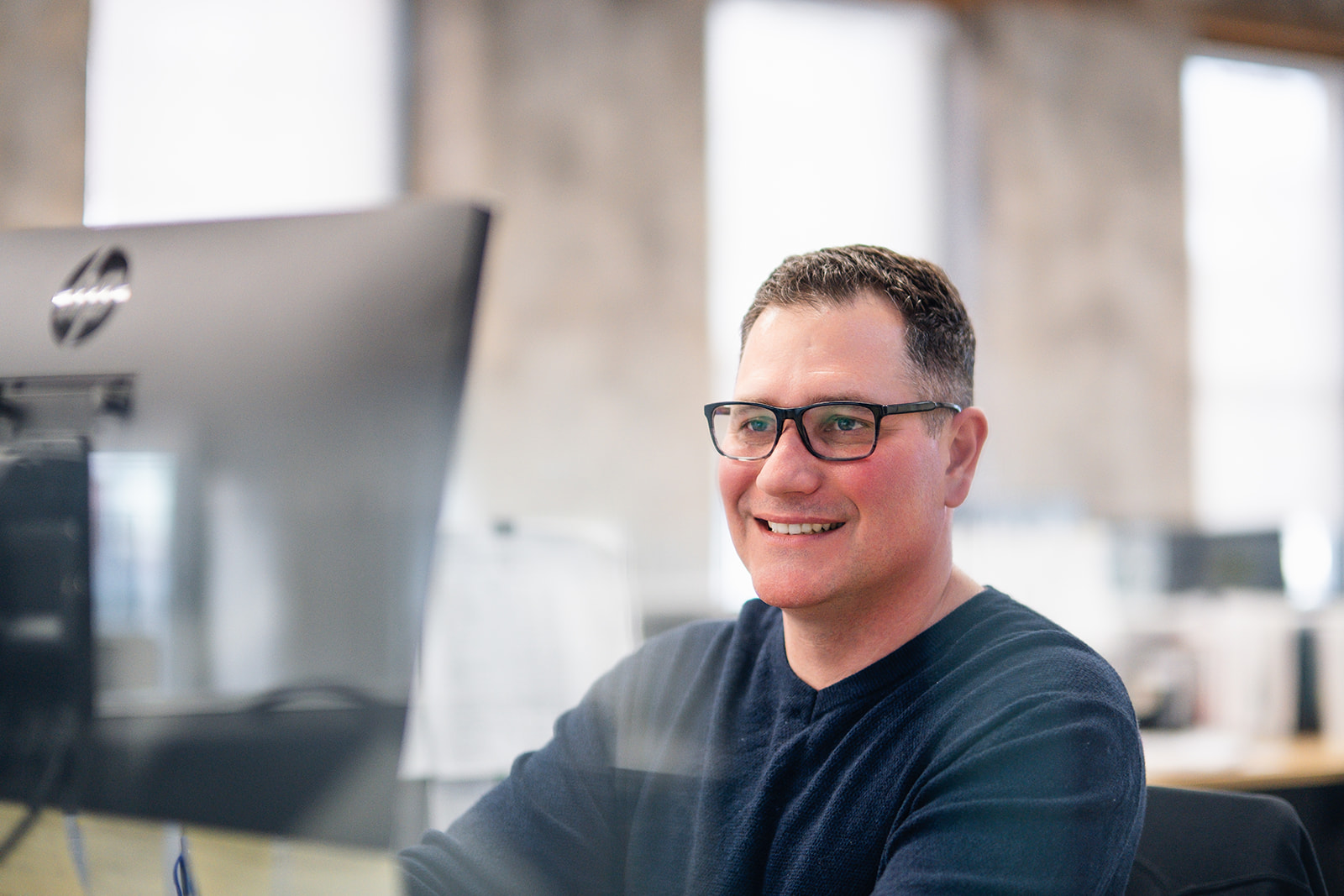 smiling man in blue shirt with glasses looking at a computer screen