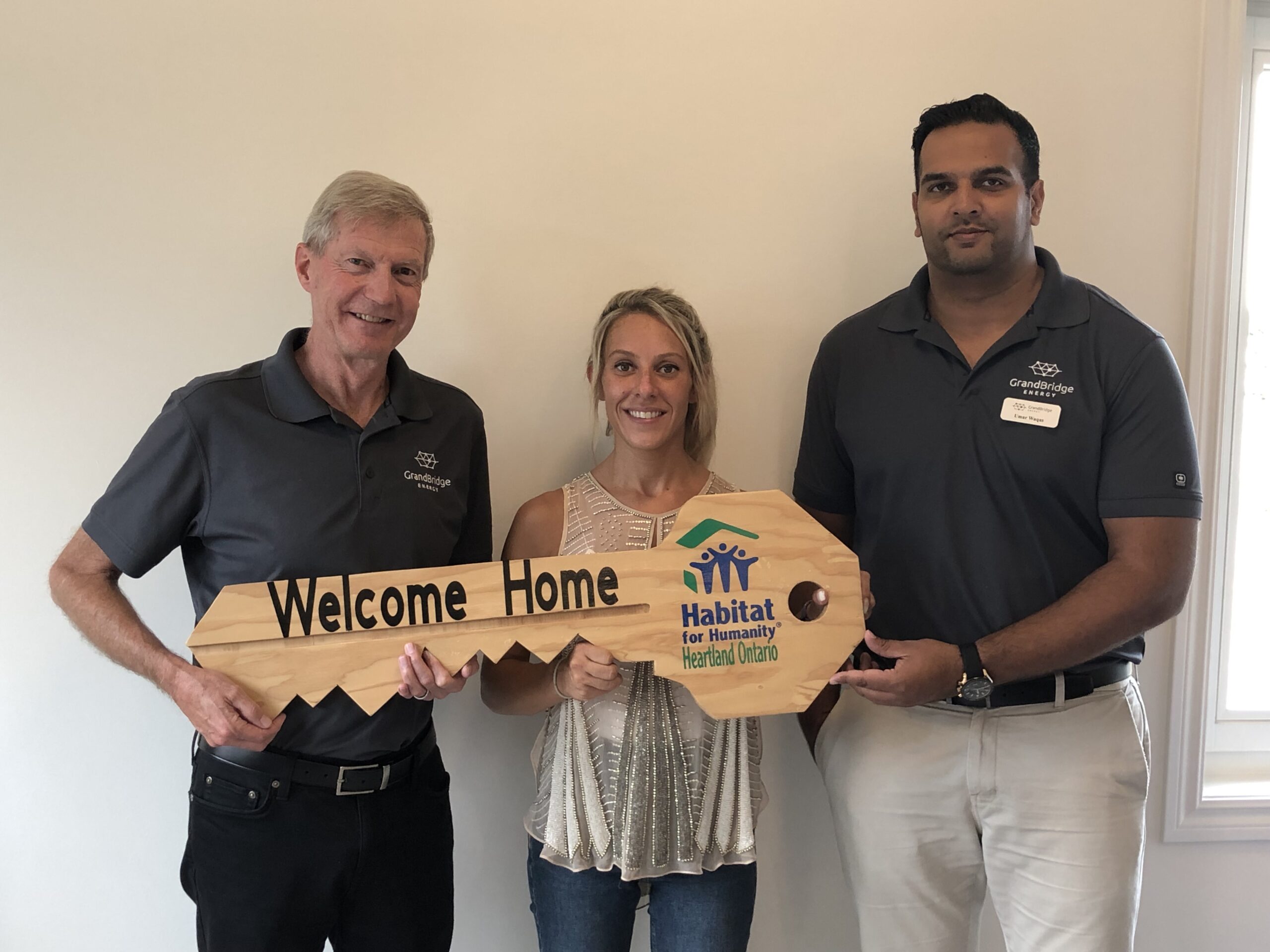 Three people hold a large wooden commemorative key with the Habitat for Humanity logo on it.