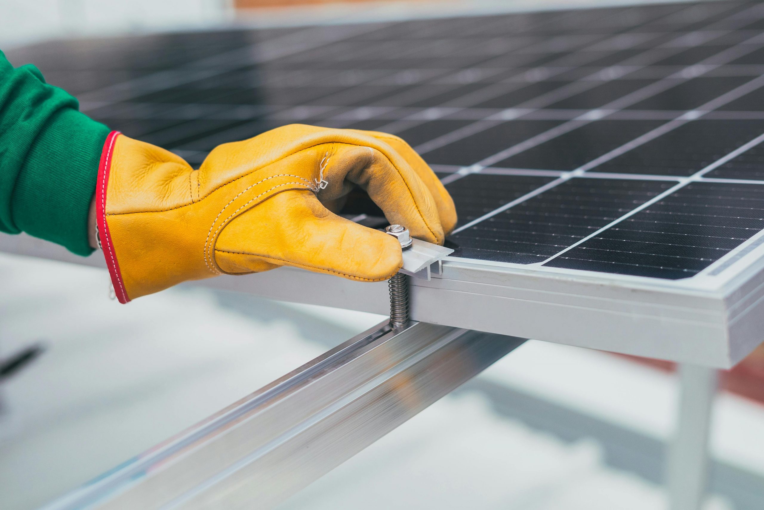 Yellow gloved hand with green sweatshirt installing a screen on a solar array panel