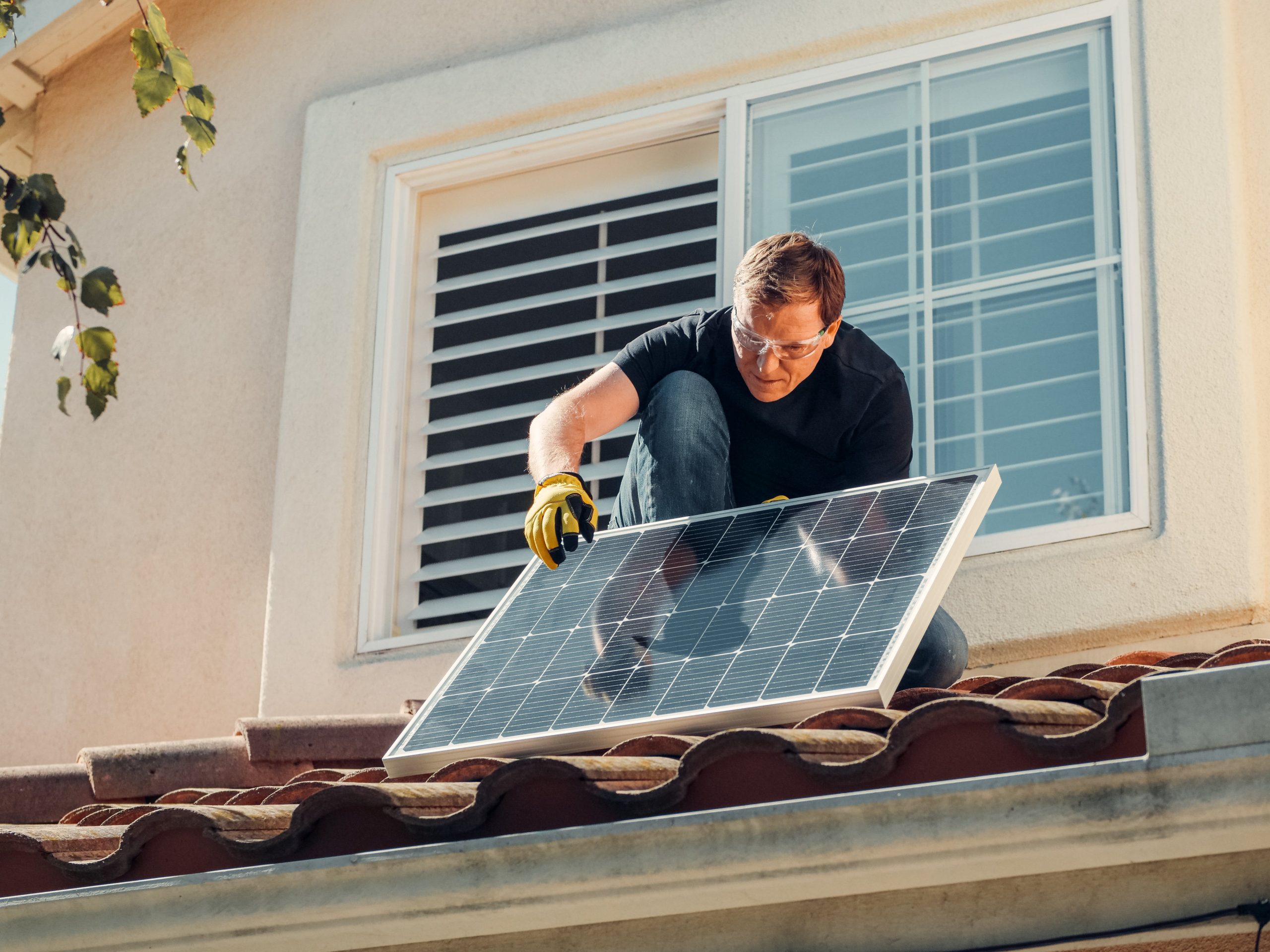 A man squats on a residential roof while installing solar panels