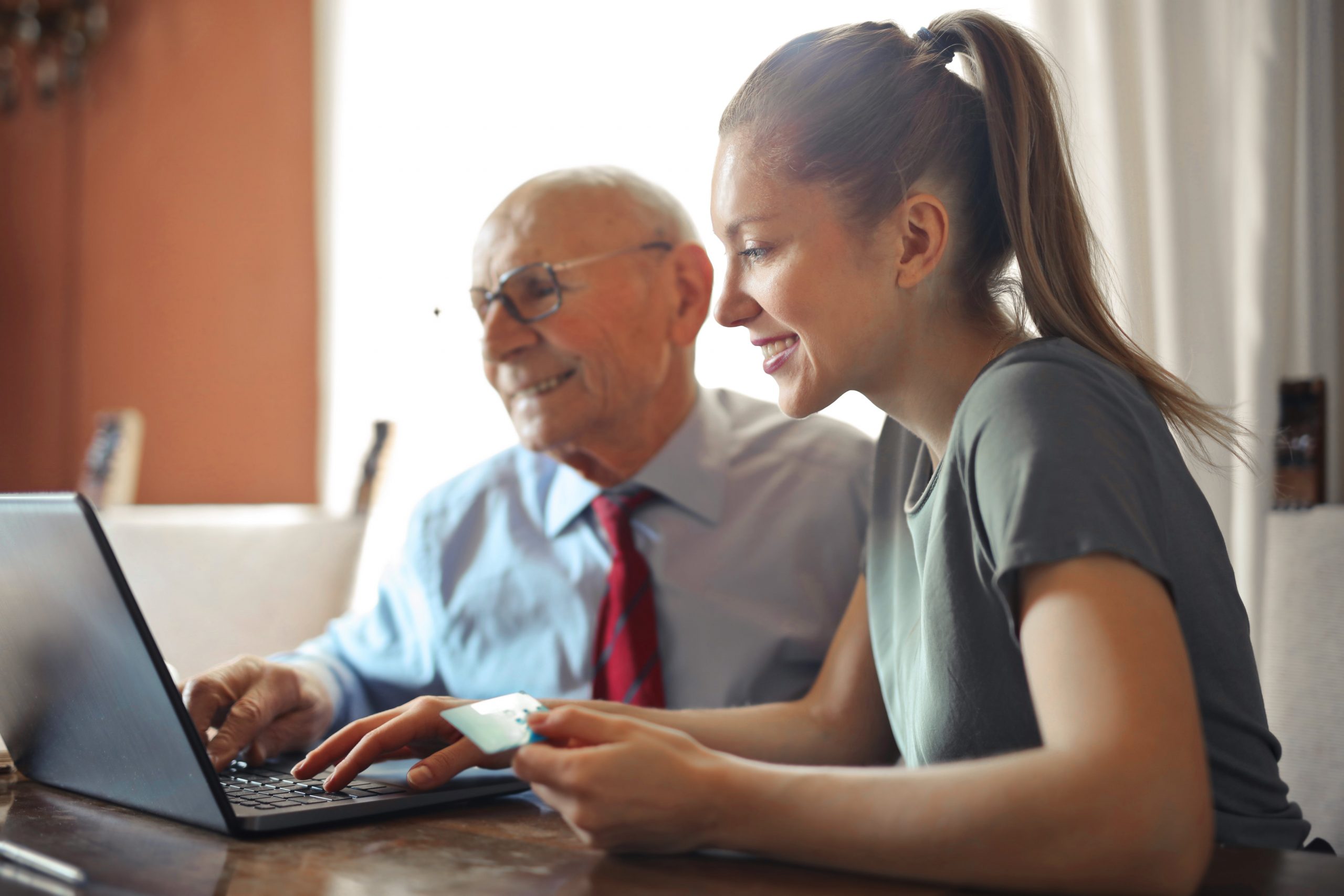 An older man and younger woman setting up automatic payments online with a laptop using their credit card.