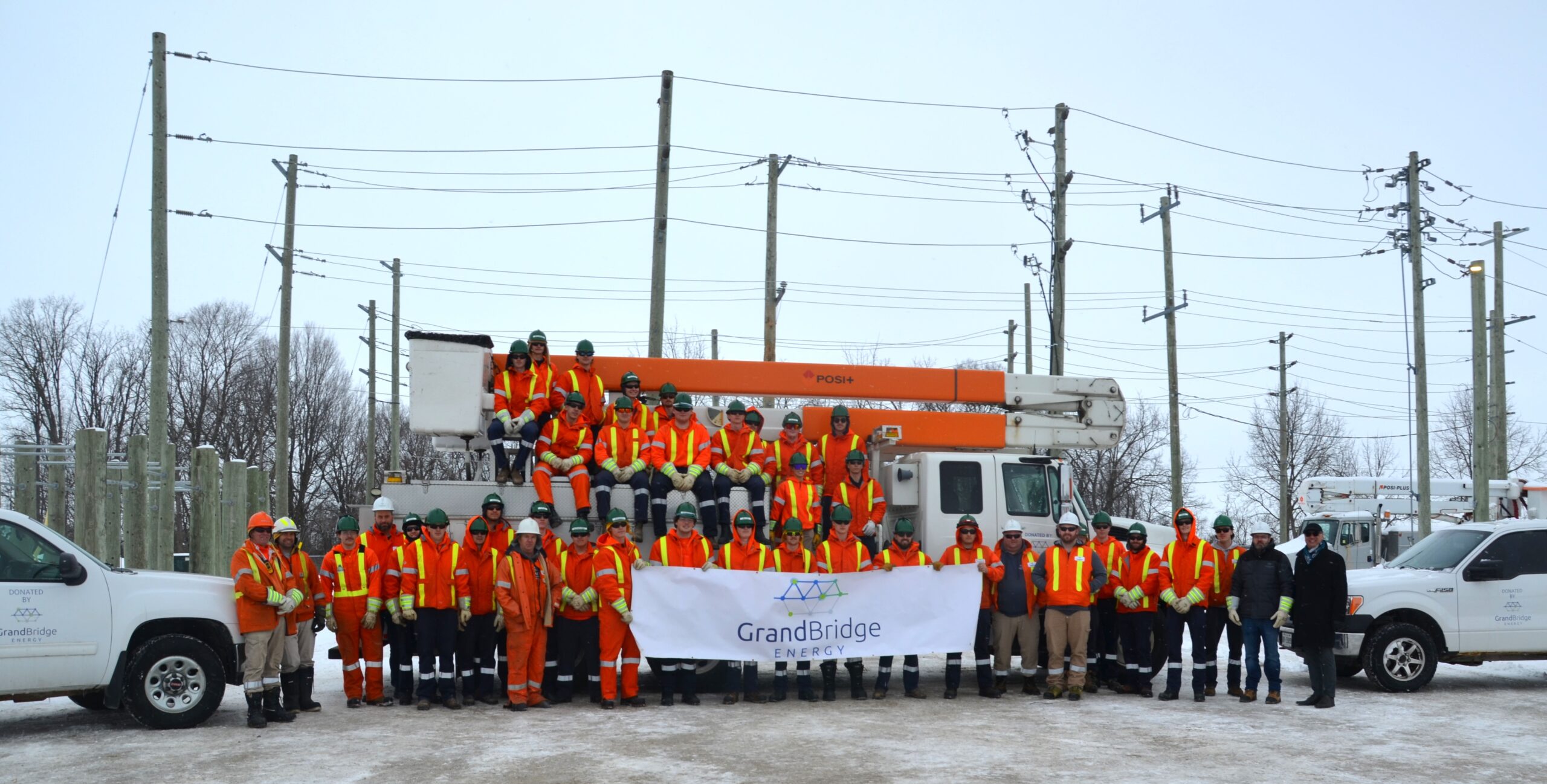 Powerline Technician Students from Conestoga College lining up infront of donated bucket truck and holding a GrandBridge Energy banner.