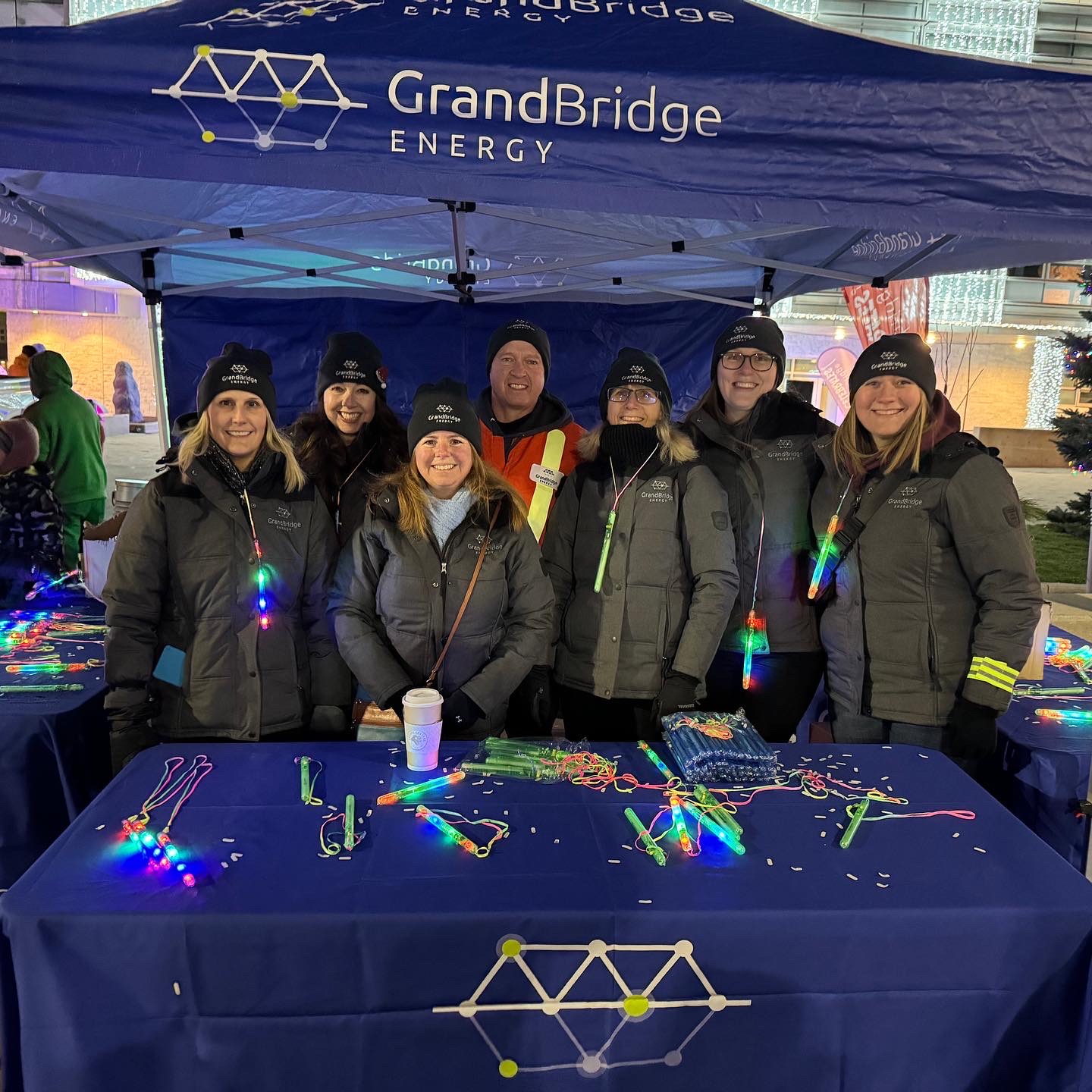 A group of employees at a nighttime winter event, under a canopy and handing out branded light sticks.