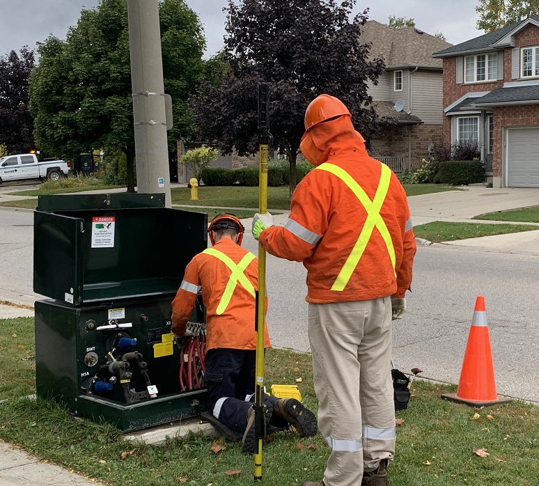 Two workers perform maintenance on a neighbourhood transformer box.