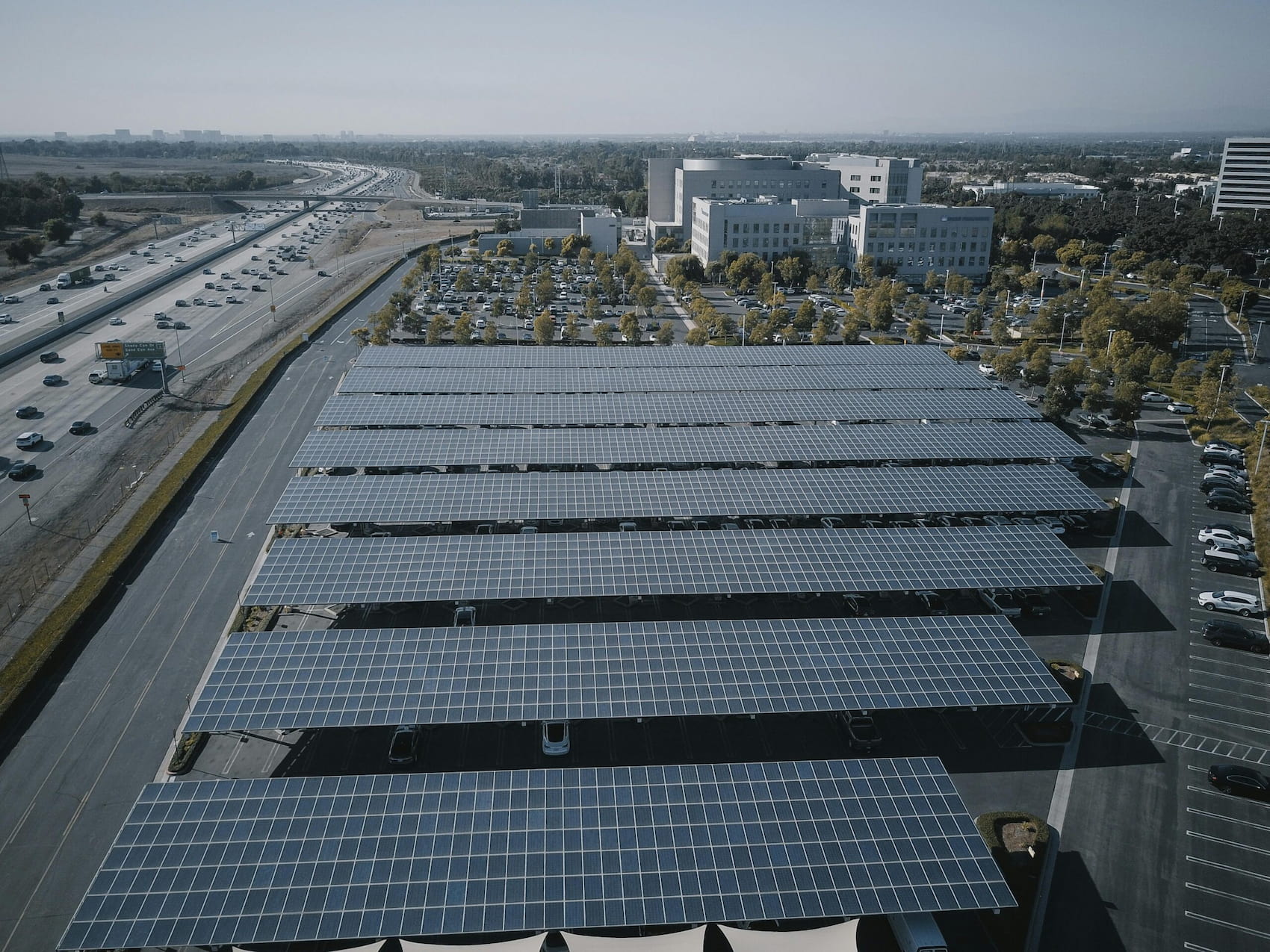 Rows of solar panels surrounded by buildings and a highway