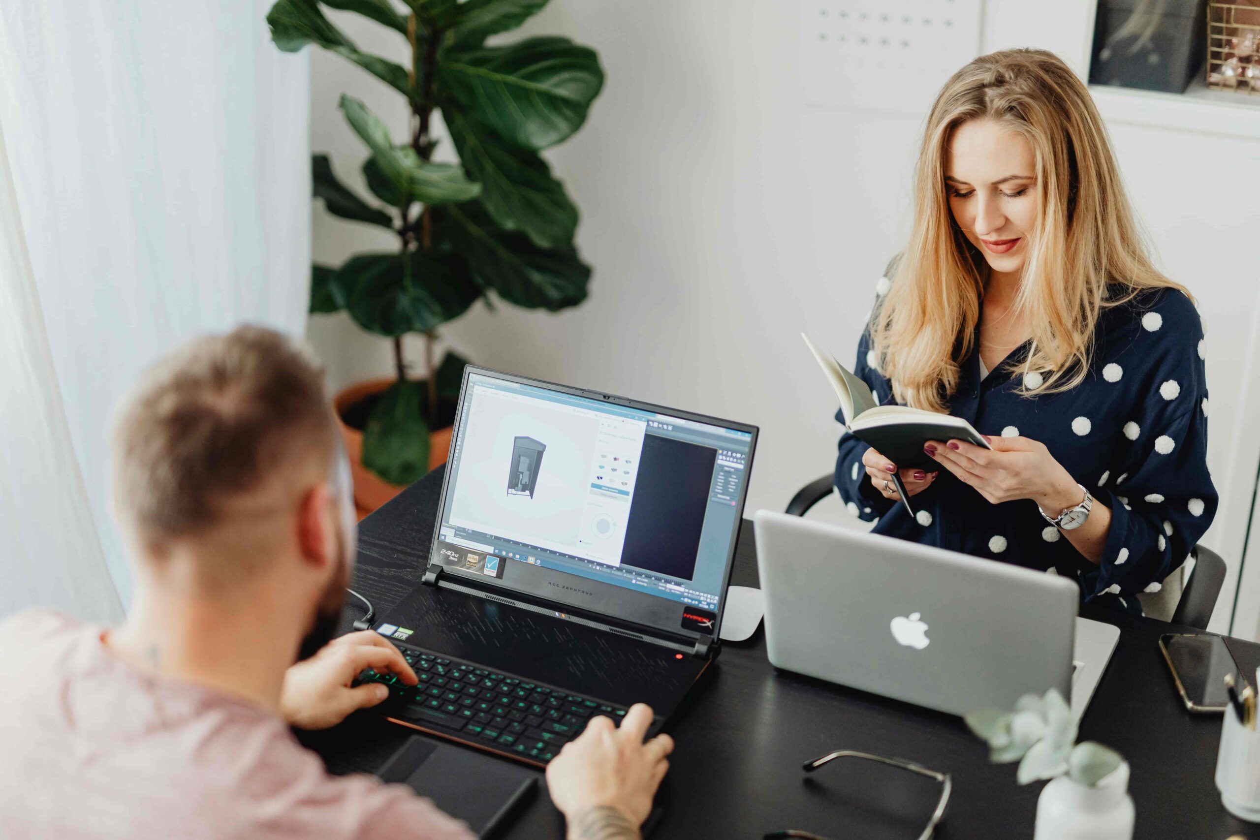 A couple sits at a table, working on laptop computers.