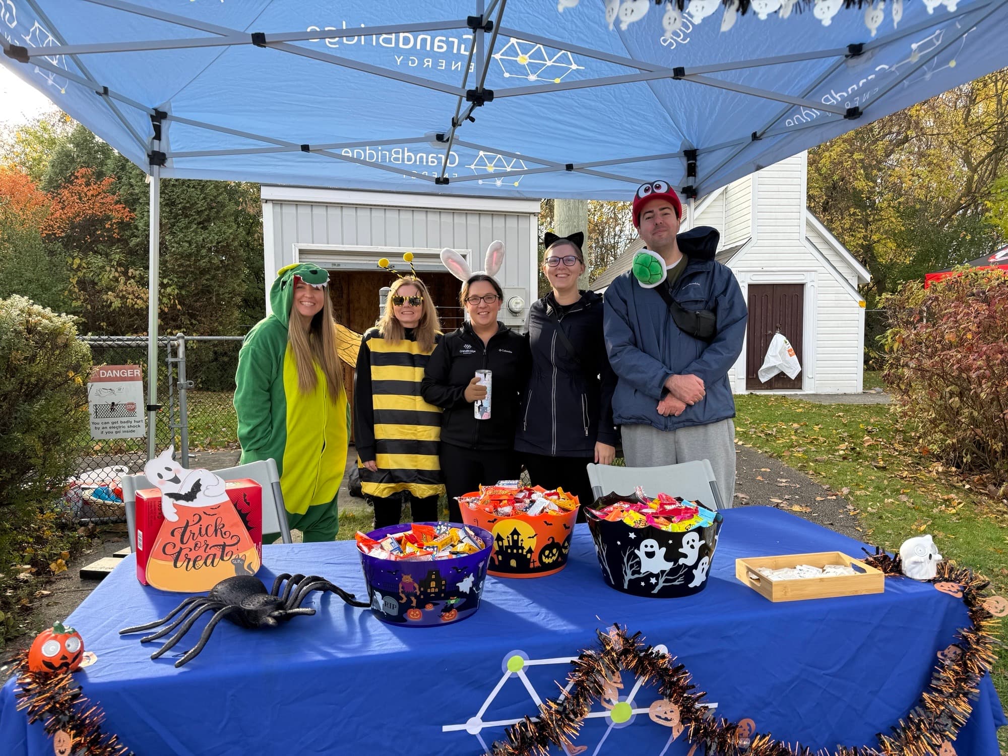 Employees dressed up for Halloween under a company tent with bowls of candy.