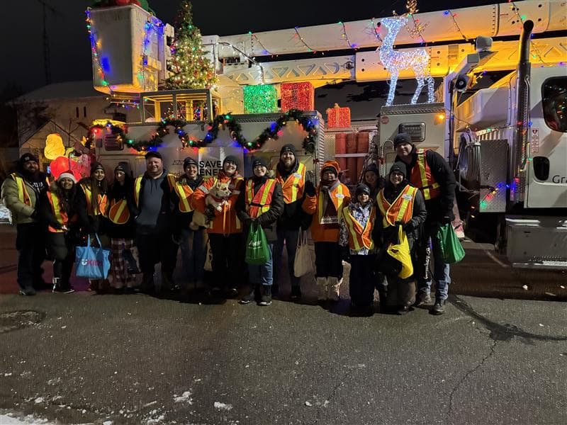Employees at night, standing infront of a decorated bucket truck for a Santa parade.