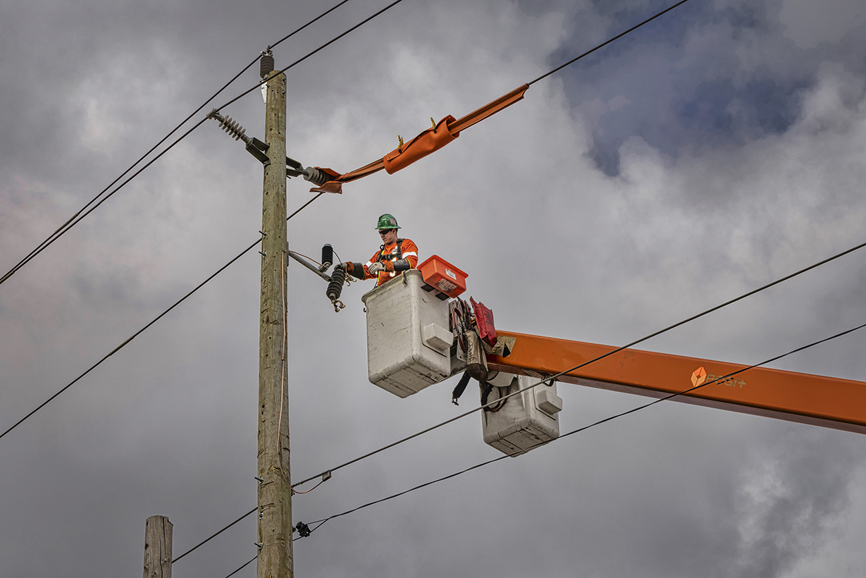 Powerline worker repairing a service with safety covers over the powerline.
